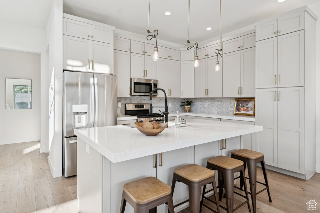 Kitchen featuring stainless steel appliances, recessed lighting, tasteful backsplash, light wood-style flooring, and a kitchen bar
