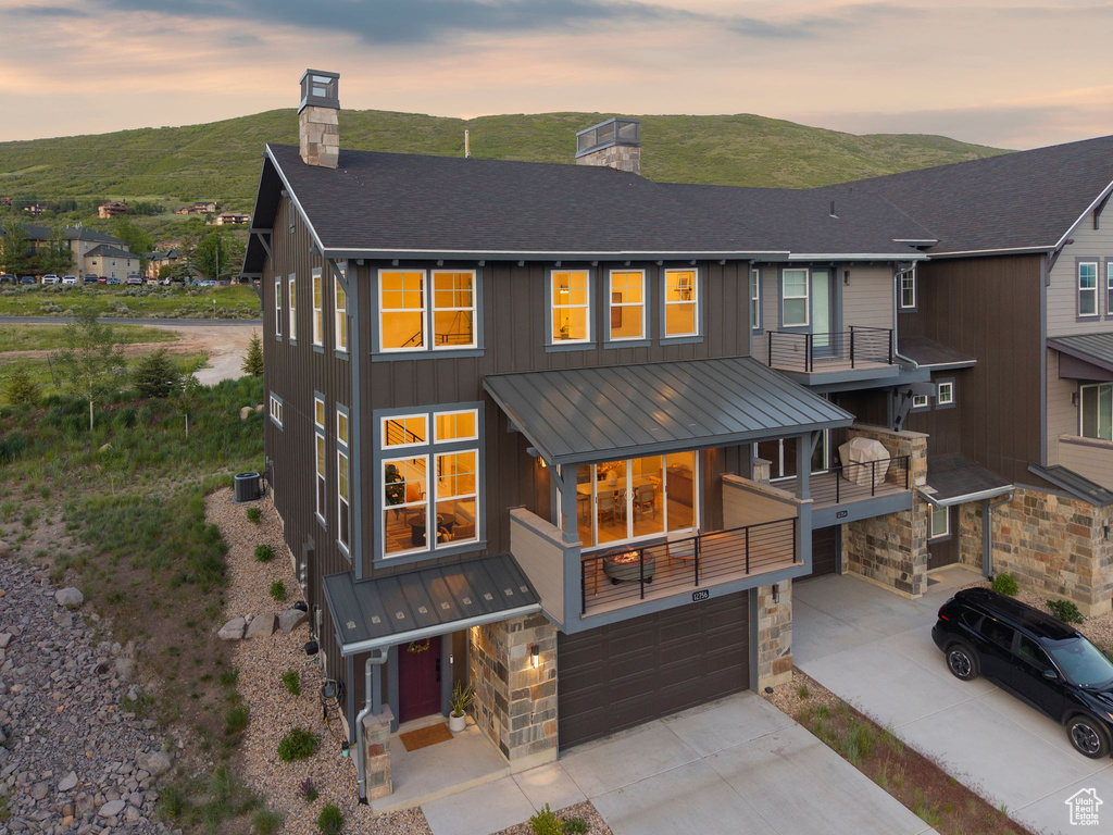 Back of property at dusk with a chimney, a standing seam roof, an attached garage, driveway, and a metal roof