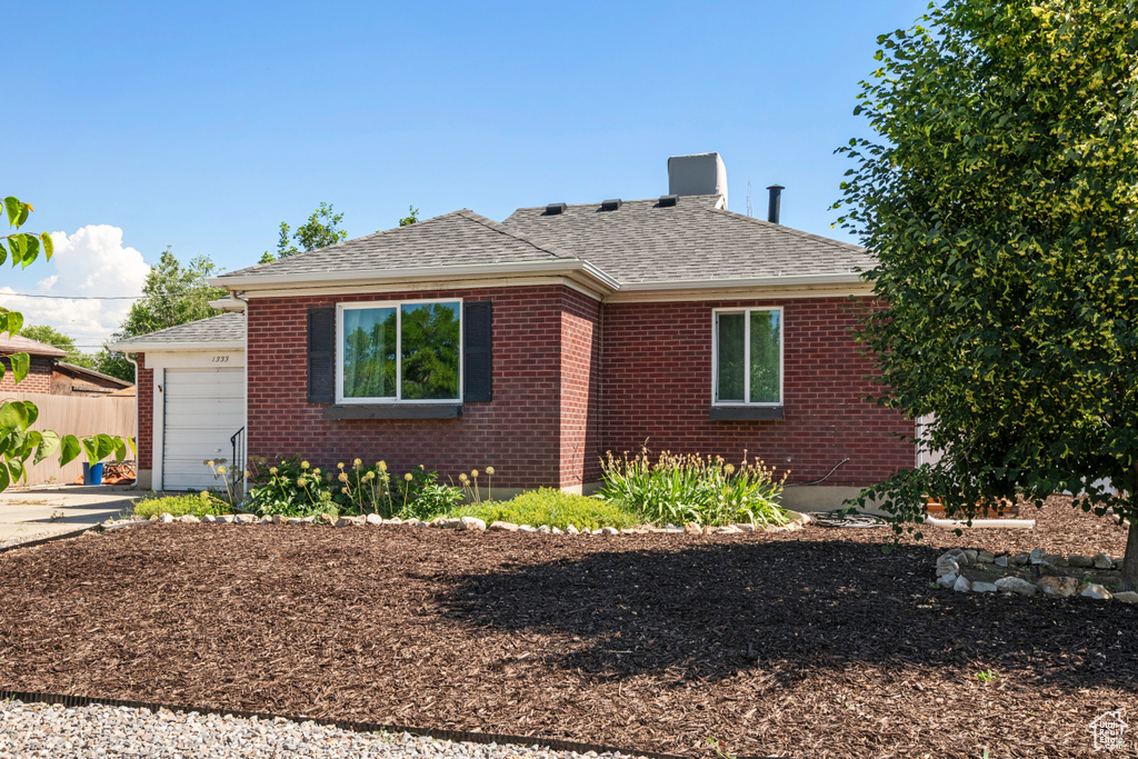 View of front of property featuring a shingled roof, brick siding, a garage, and driveway