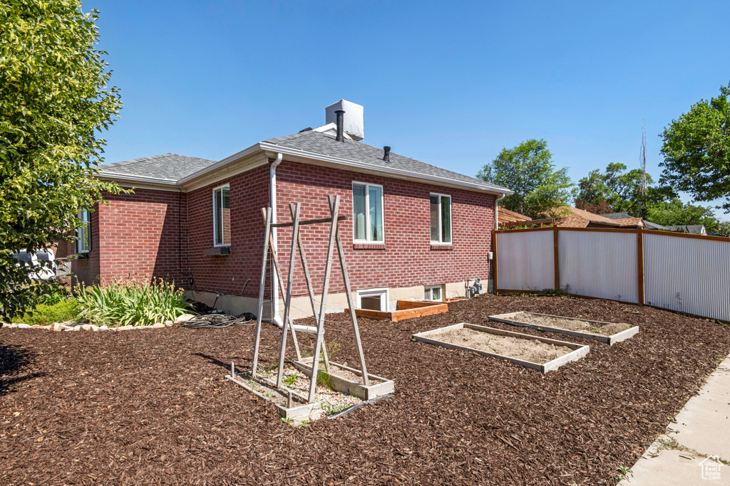 Back of house featuring brick siding, a garden, roof with shingles, and a chimney