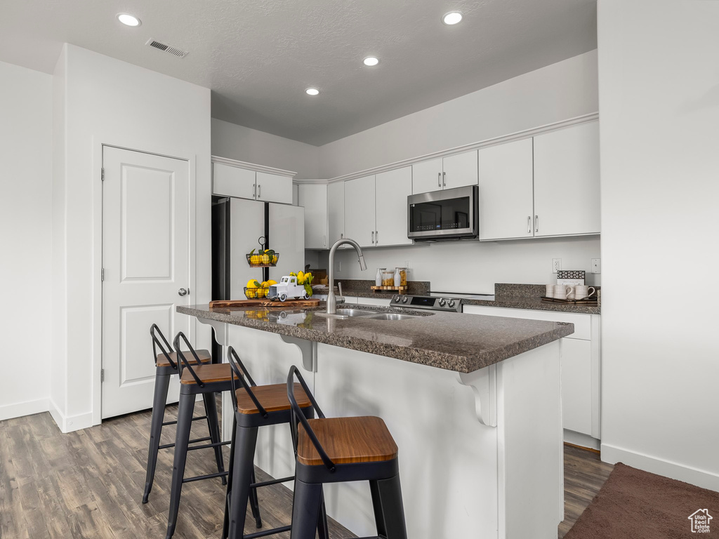 Kitchen featuring stainless steel microwave, freestanding refrigerator, dark wood-type flooring, white cabinets, and recessed lighting