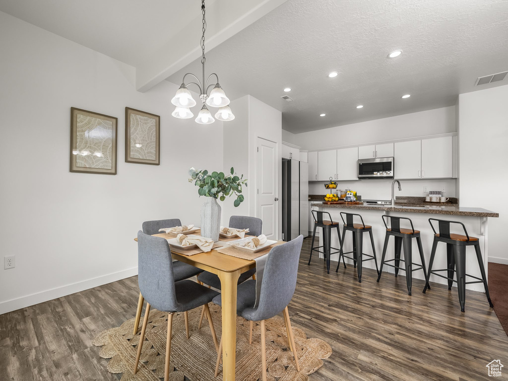 Dining space with dark wood-type flooring, recessed lighting, a chandelier, a textured ceiling, and beam ceiling