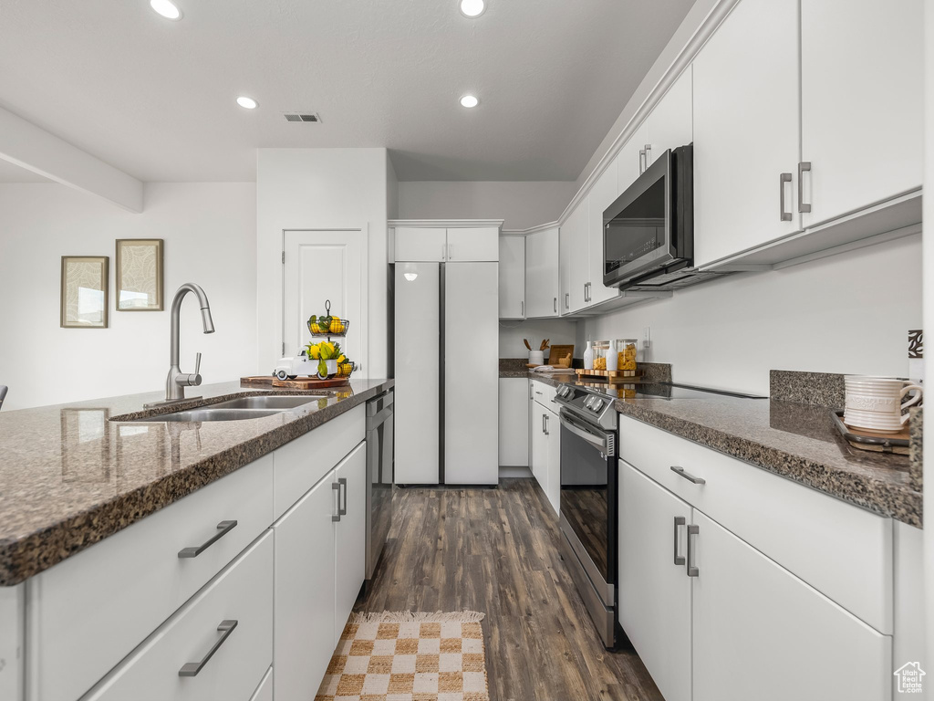 Kitchen with stainless steel appliances, recessed lighting, white cabinets, dark stone counters, and dark wood finished floors