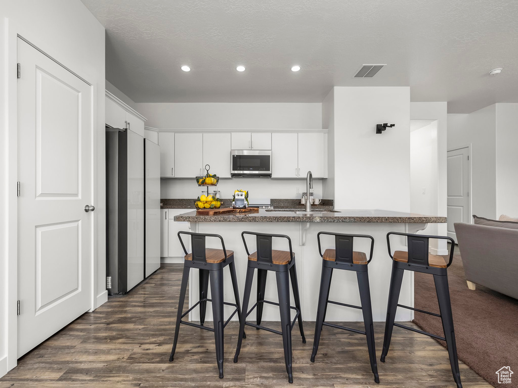 Kitchen with stainless steel appliances, dark countertops, a kitchen breakfast bar, recessed lighting, and white cabinets