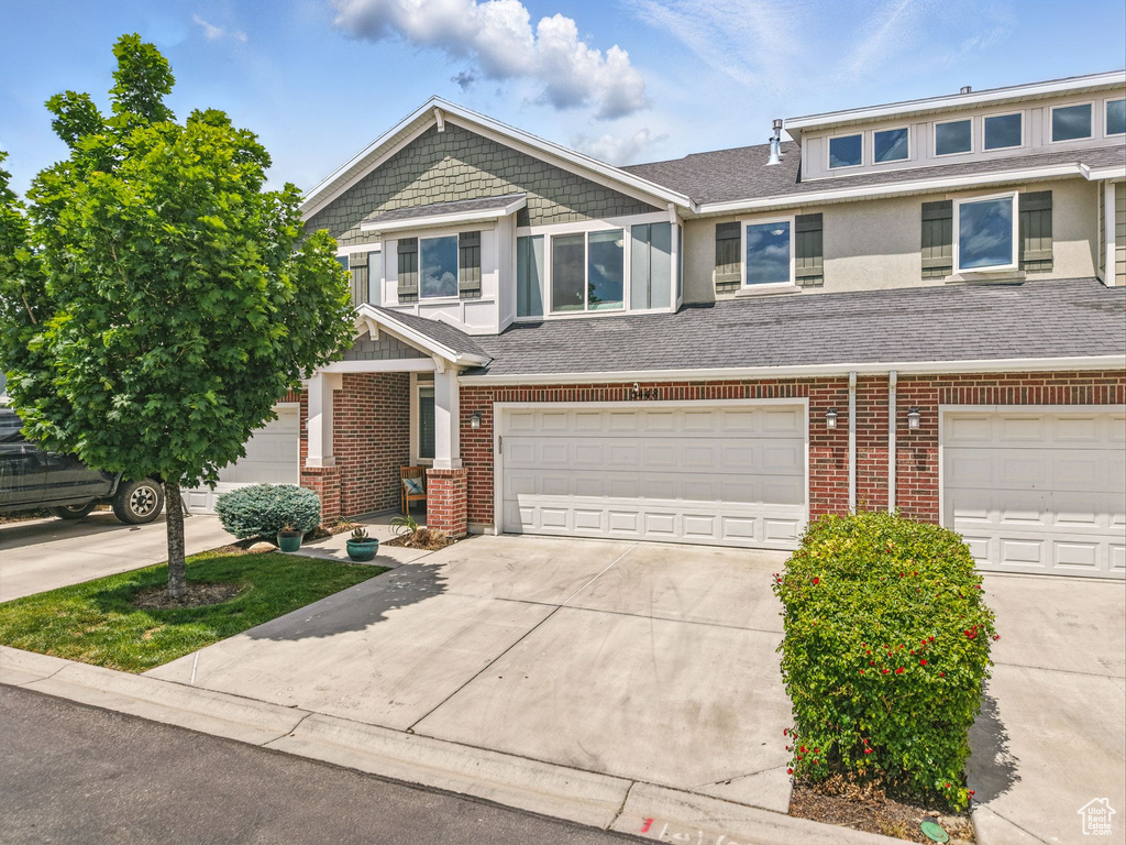 View of property featuring a garage, concrete driveway, brick siding, and a shingled roof
