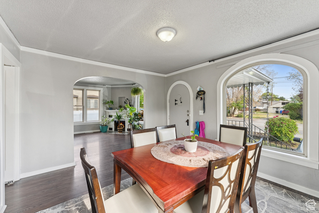 Dining room featuring arched walkways, a textured ceiling, wood finished floors, and ornamental molding