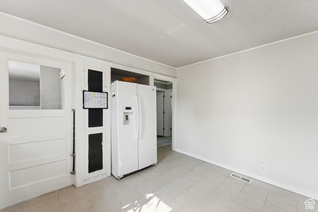 Unfurnished bedroom with white fridge with ice dispenser and light tile patterned floors