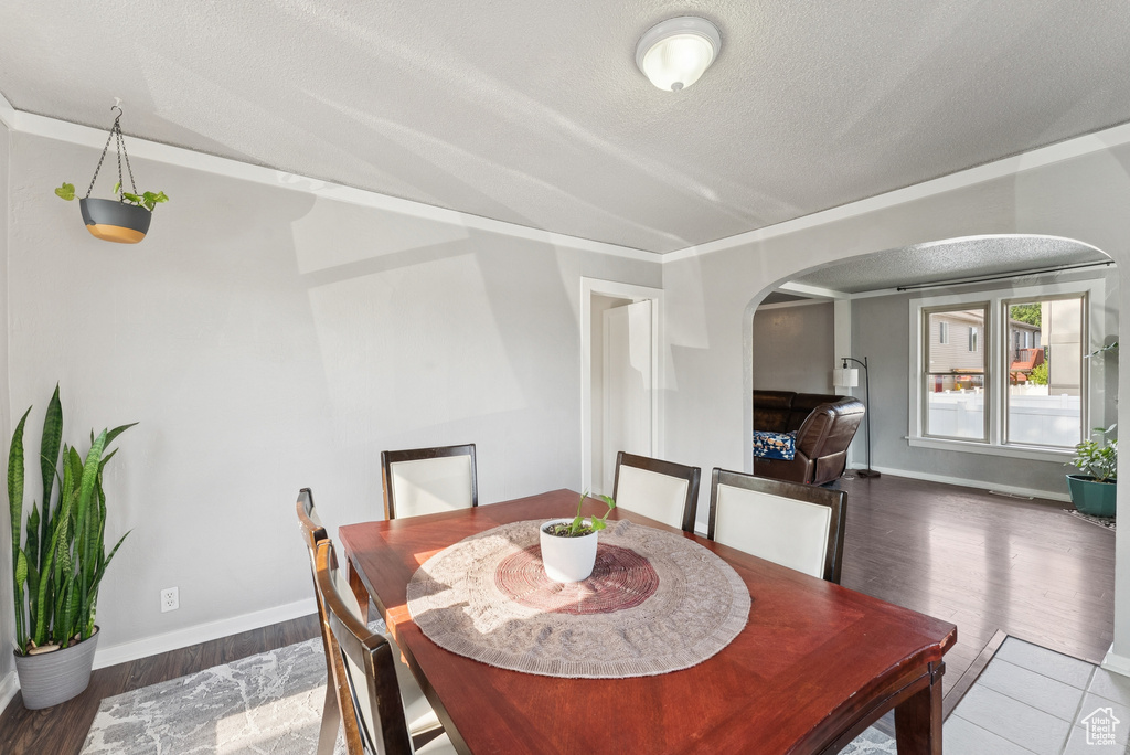 Dining space with arched walkways, wood finished floors, and a textured ceiling