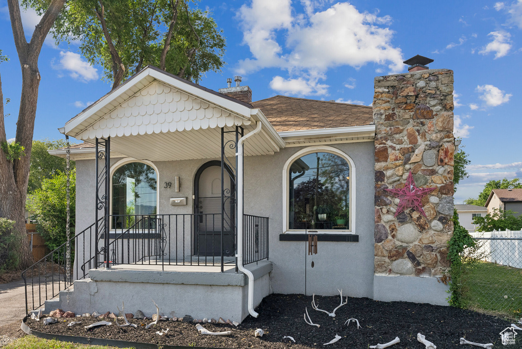 View of front of house featuring a chimney, stucco siding, a porch, and a shingled roof