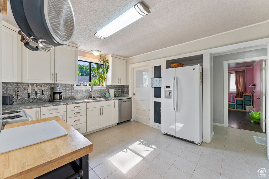 Kitchen with white fridge with ice dispenser, stainless steel dishwasher, light tile patterned floors, decorative backsplash, and a textured ceiling