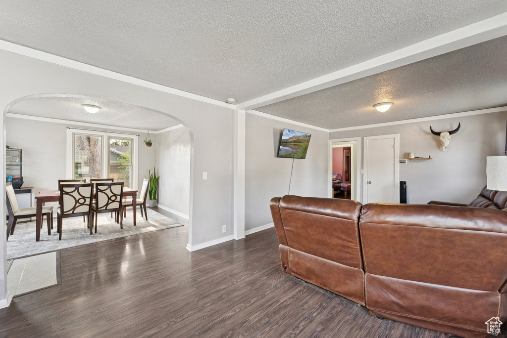 Living area featuring arched walkways, a textured ceiling, wood finished floors, and crown molding