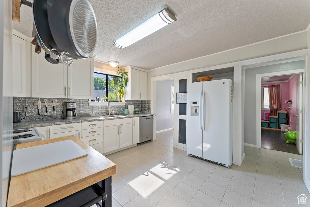 Kitchen with white fridge with ice dispenser, dishwasher, light tile patterned floors, decorative backsplash, and white cabinetry