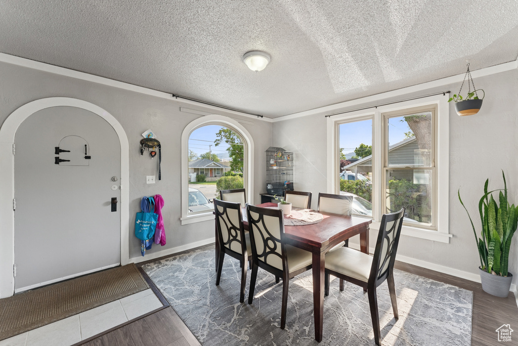 Dining area featuring wood finished floors, healthy amount of natural light, arched walkways, a textured ceiling, and ornamental molding