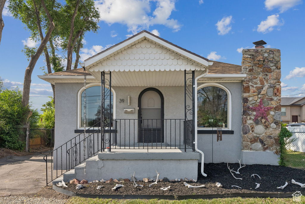 View of front of home with stucco siding, roof with shingles, a porch, and a chimney