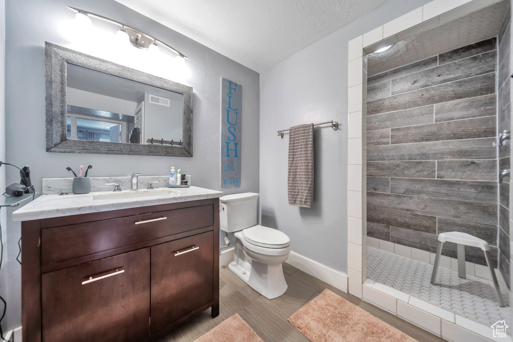 Full bathroom featuring a walk in shower, vanity, wood finished floors, and a textured ceiling