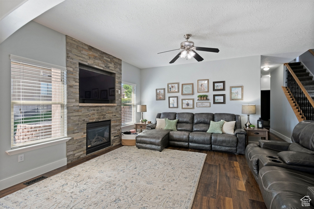Living area with stairs, a ceiling fan, dark wood-style floors, a fireplace, and a textured ceiling