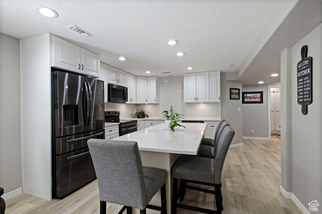 Kitchen with black appliances, light wood finished floors, a kitchen bar, white cabinetry, and recessed lighting