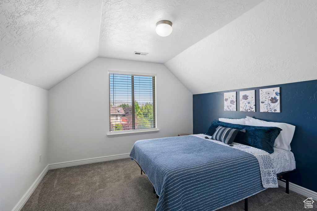 Carpeted bedroom featuring a textured ceiling and vaulted ceiling