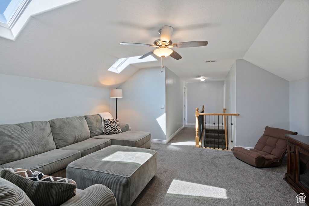 Carpeted living area with a skylight, vaulted ceiling, and a ceiling fan