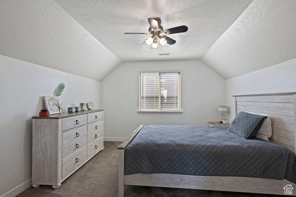 Bedroom with a textured ceiling, lofted ceiling, dark colored carpet, and a ceiling fan
