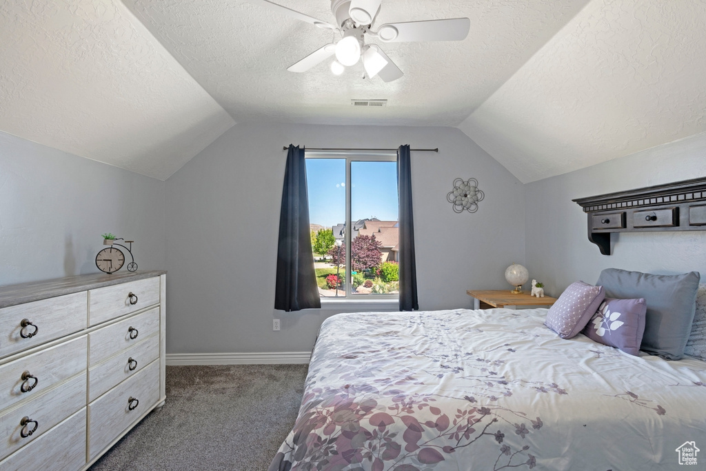 Carpeted bedroom featuring a textured ceiling, vaulted ceiling, and a ceiling fan