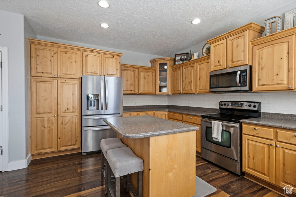 Kitchen featuring appliances with stainless steel finishes, a center island, glass insert cabinets, dark wood-style floors, and a textured ceiling