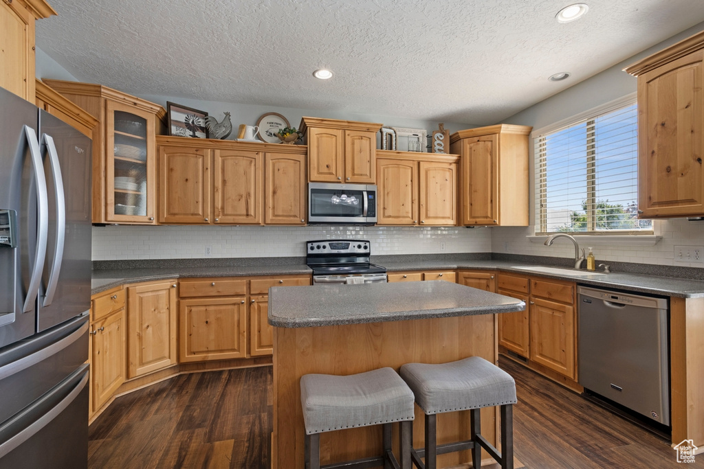 Kitchen with appliances with stainless steel finishes, dark wood-type flooring, a textured ceiling, a center island, and a kitchen breakfast bar