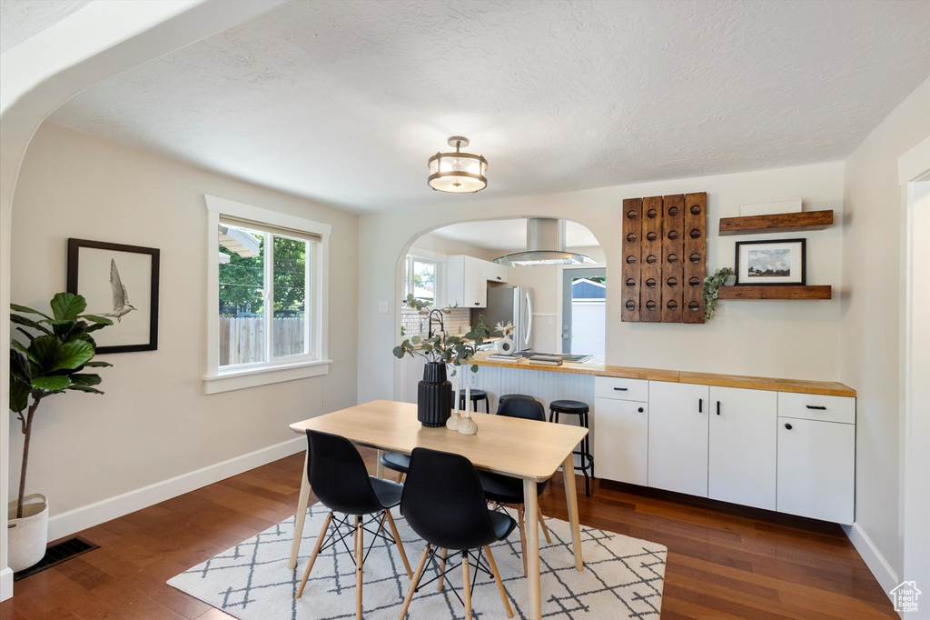 Dining space featuring arched walkways, dark wood-style flooring, and a textured ceiling