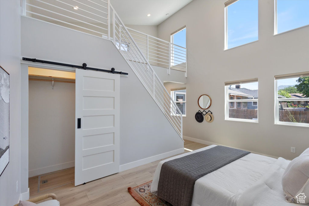 Bedroom featuring a barn door, light wood-type flooring, a towering ceiling, and recessed lighting