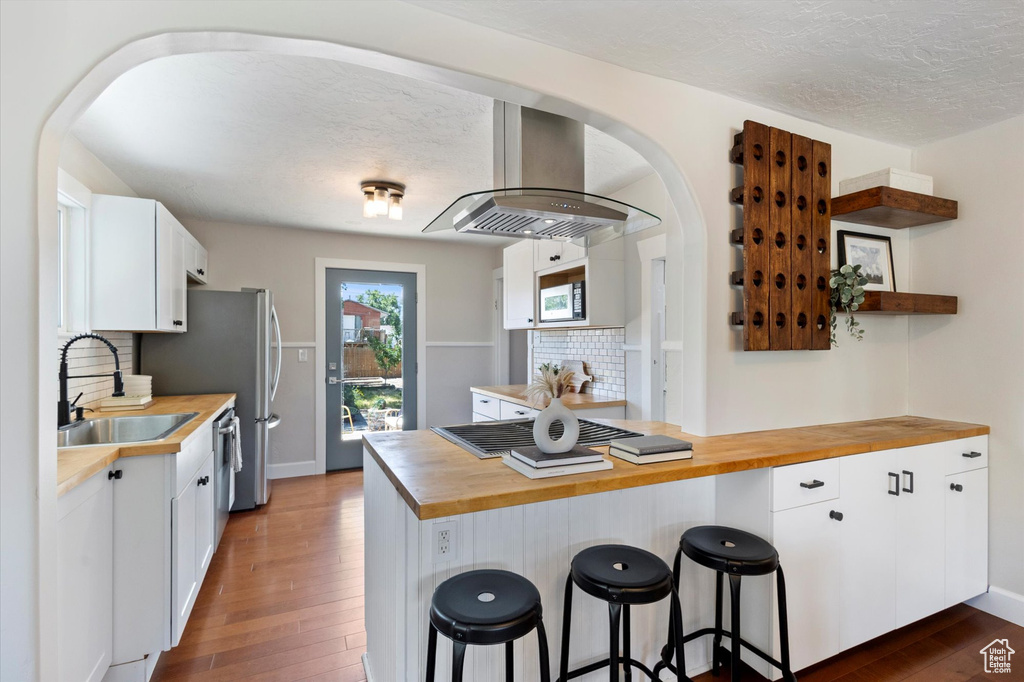 Kitchen with butcher block countertops, island exhaust hood, dark wood-style flooring, white microwave, and decorative backsplash