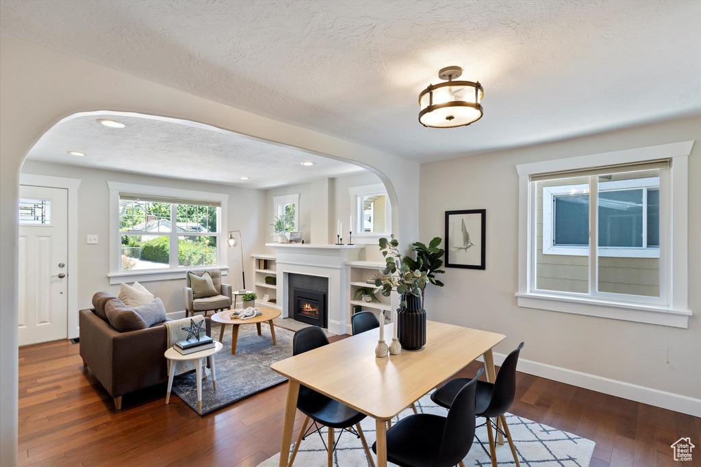 Dining area with arched walkways, dark wood-style floors, a glass covered fireplace, a textured ceiling, and recessed lighting