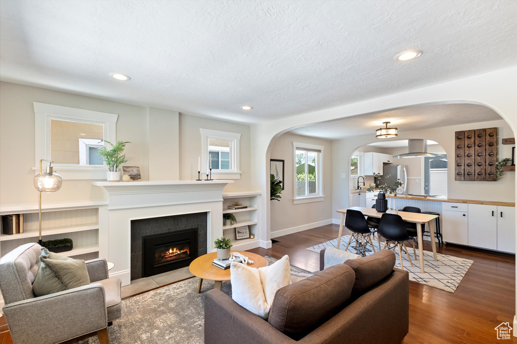 Living area with arched walkways, a fireplace with flush hearth, wood finished floors, recessed lighting, and a textured ceiling