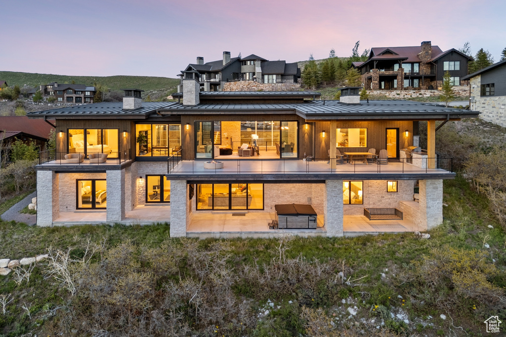 Back of property at dusk featuring a standing seam roof, a chimney, a patio area, a metal roof, and a balcony