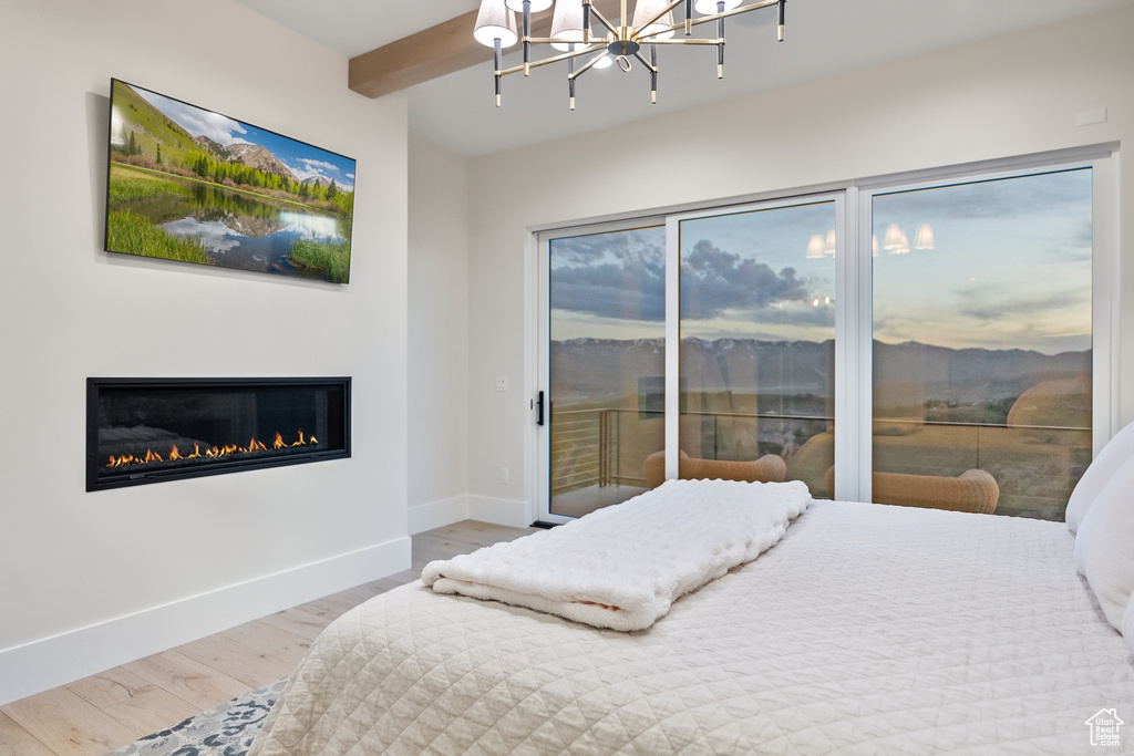 Bedroom featuring access to outside, a chandelier, wood finished floors, a glass covered fireplace, and beam ceiling