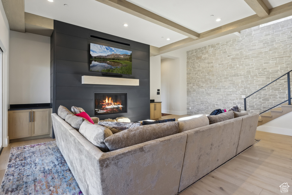 Living room featuring a fireplace, light wood finished floors, beam ceiling, stairway, and recessed lighting