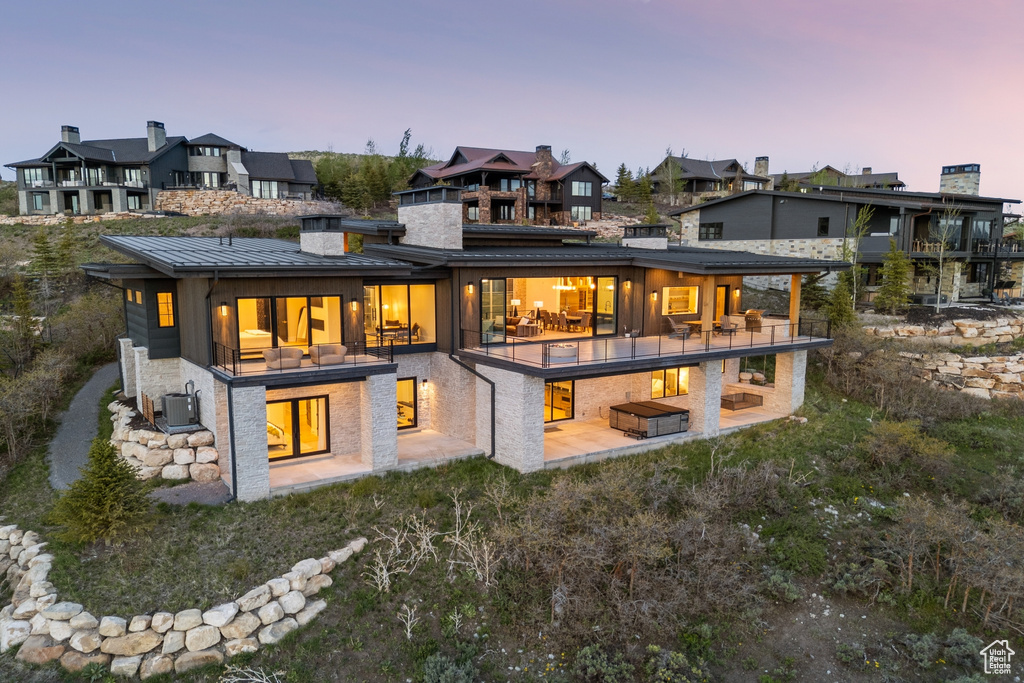 Back of property at dusk featuring a patio area, a chimney, a standing seam roof, and a residential view