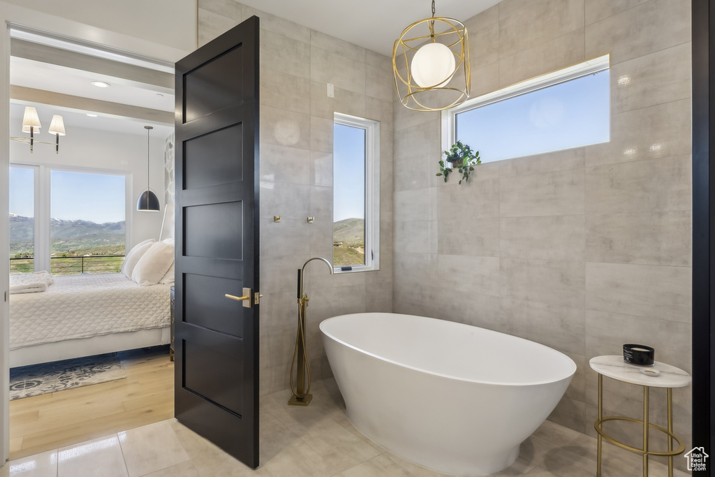 Bathroom featuring tile walls, a freestanding bath, ensuite bathroom, and a chandelier