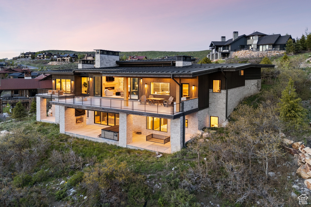 Back of property at dusk with a balcony, a patio, a standing seam roof, a chimney, and a metal roof
