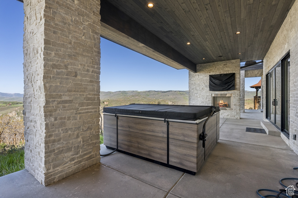 View of patio with an outdoor stone fireplace, a mountain view, and a hot tub