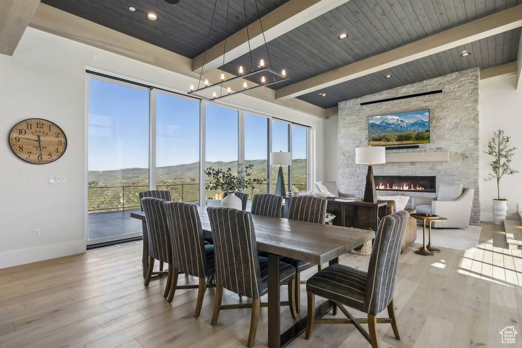 Dining area with light wood-style flooring, a fireplace, and a wooden ceiling with exposed beams