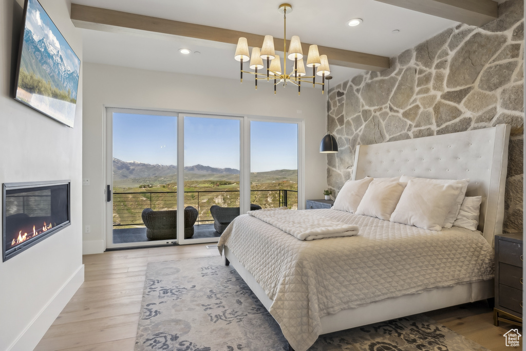 Bedroom featuring beamed ceiling, a mountain view, access to exterior, wood finished floors, and a chandelier
