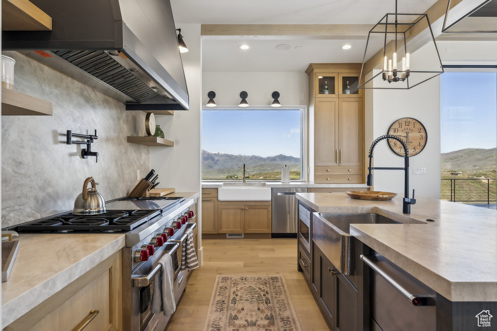 Kitchen with wall chimney range hood, appliances with stainless steel finishes, light wood-style floors, light countertops, and light brown cabinets