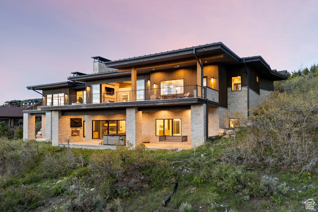 Back of house featuring a balcony, a chimney, and a patio
