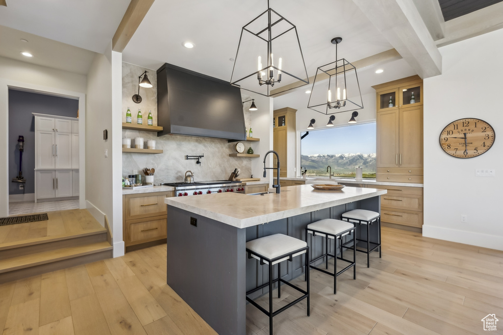 Kitchen with custom exhaust hood, light countertops, tasteful backsplash, open shelves, and light wood finished floors