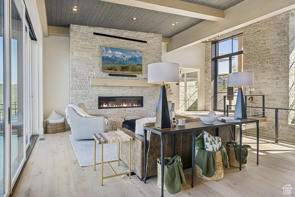 Living room featuring wood-type flooring, a stone fireplace, and a wood ceiling with exposed beams
