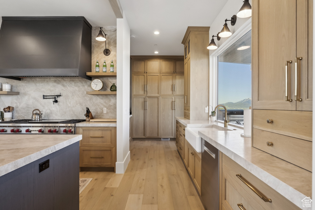 Kitchen with ventilation hood, dishwasher, light countertops, light wood-type flooring, and backsplash