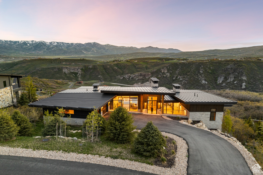 View of front of home with a standing seam roof, a mountain view, a metal roof, stone siding, and driveway