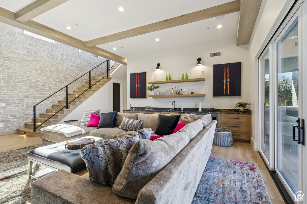 Living room with wet bar, stairway, beam ceiling, light wood finished floors, and recessed lighting