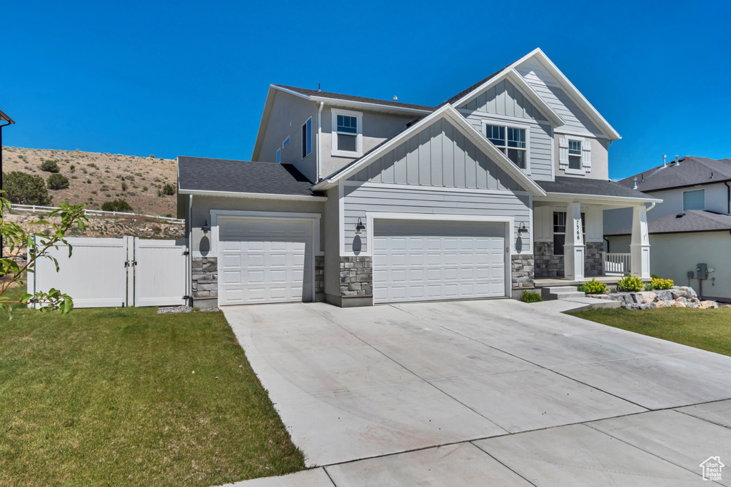View of front of house featuring a gate, driveway, board and batten siding, stone siding, and covered porch