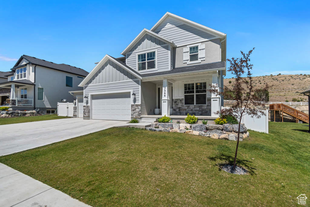 View of front facade featuring board and batten siding, covered porch, driveway, a front lawn, and stone siding